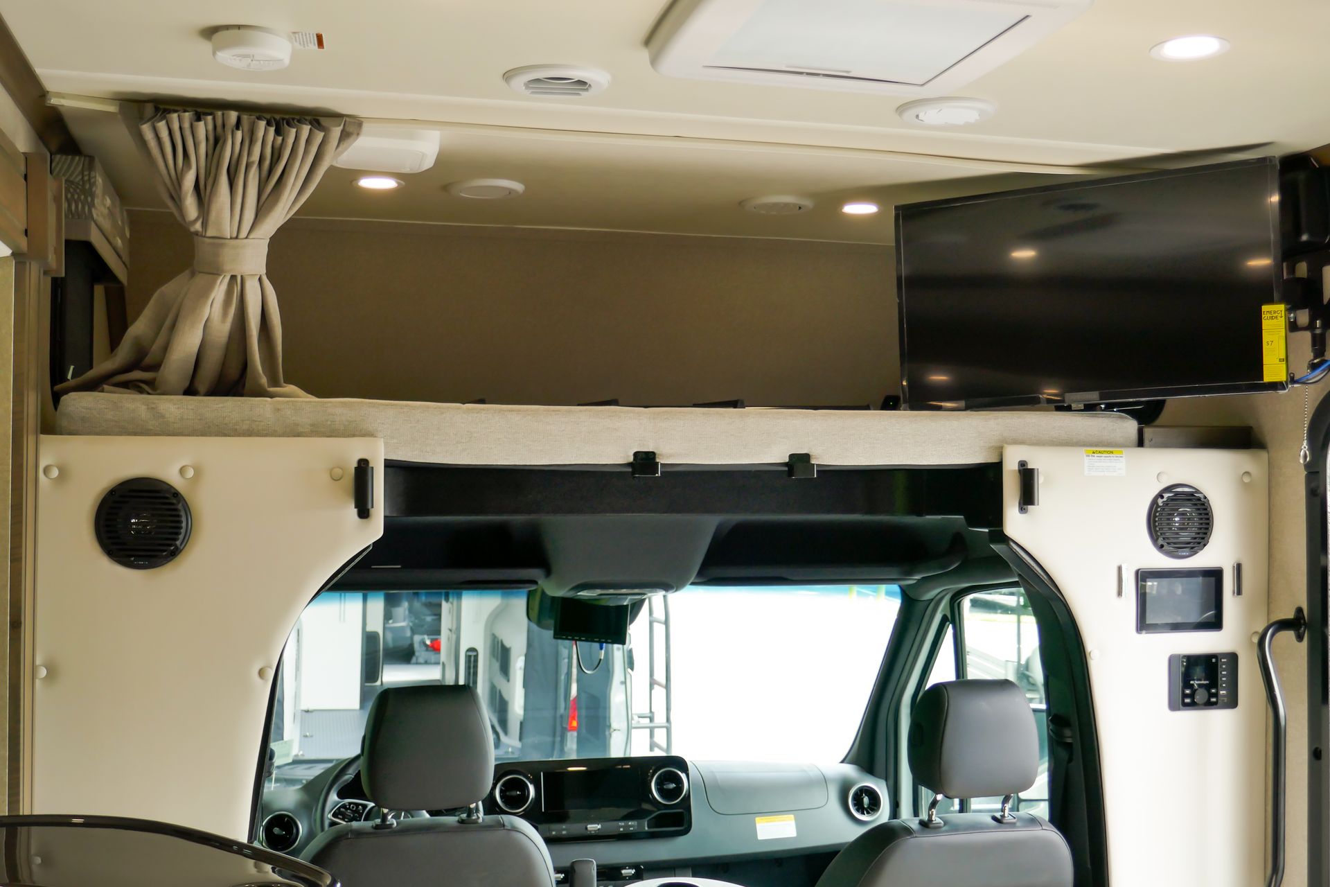 Interior view of a recreational vehicle with a bed, TV, and driver's seats. Beige and neutral tones are dominant. Interior view of a recreational vehicle with a bed, TV, and driver's seats. Beige and neutral tones are dominant.