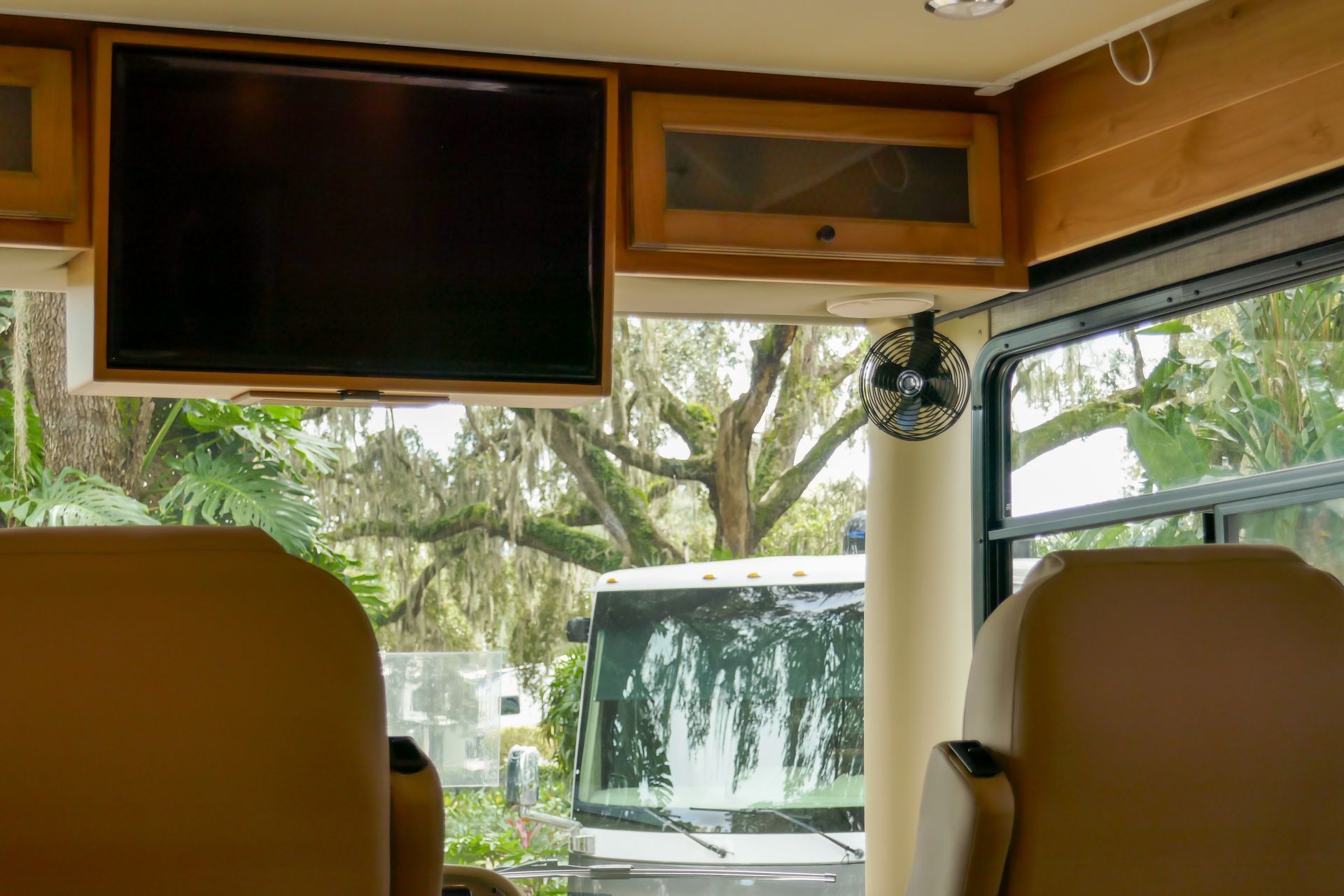 Interior of RV with TV, cabinets, and a window looking out at a tree and part of another vehicle. Interior of RV with TV, cabinets, and a window looking out at a tree and part of another vehicle.
