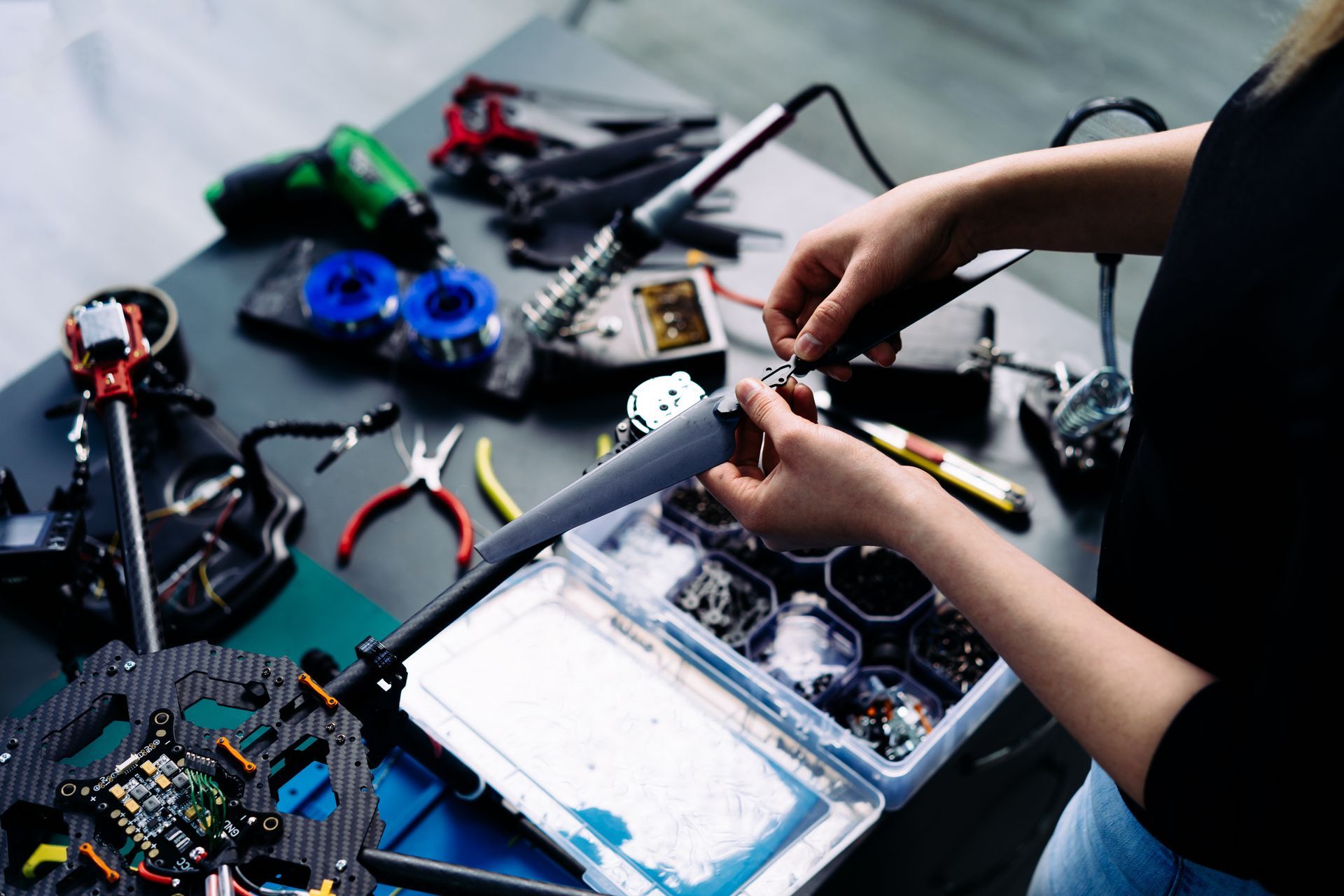 Person working on electronics, surrounded by tools and parts on a table. Person working on electronics, surrounded by tools and parts on a table.