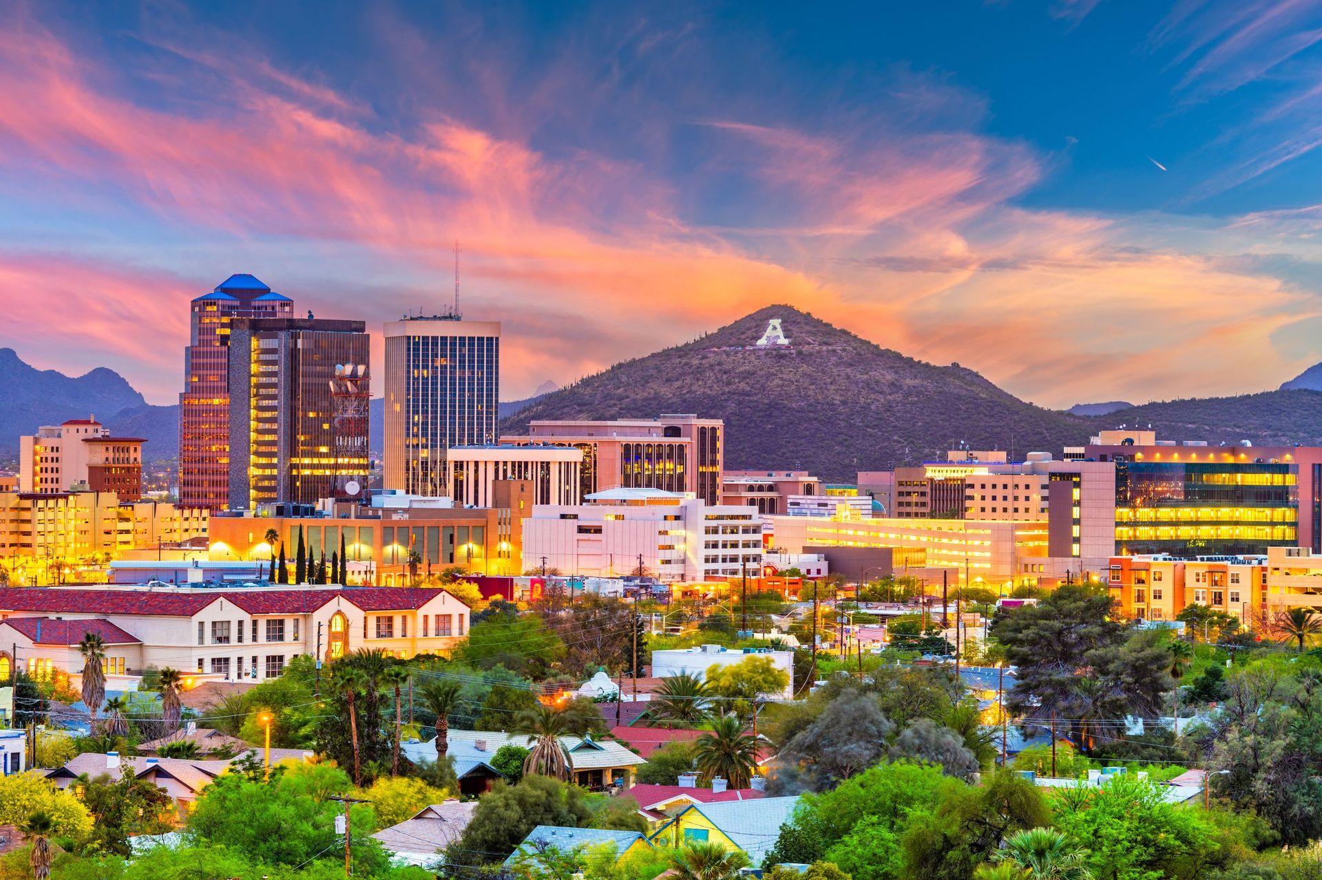 Sunset city skyline with colorful clouds, lit buildings, and a mountain backdrop