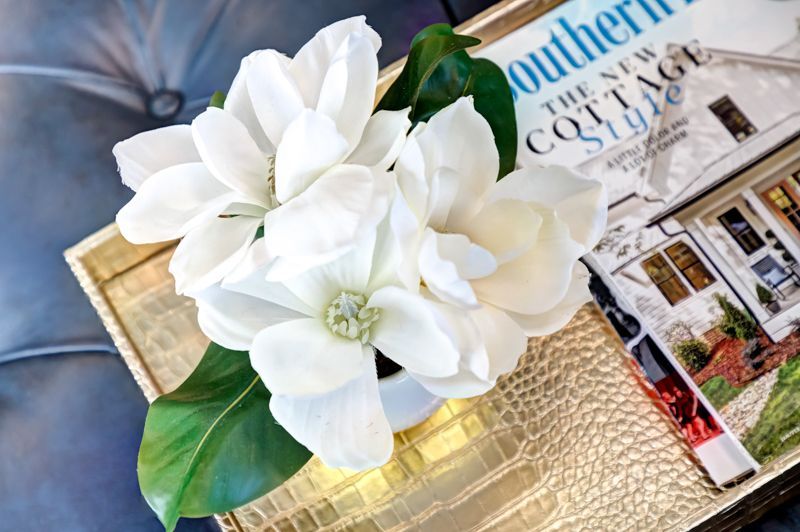 Two white flowers are sitting on top of a gold tray next to a magazine.