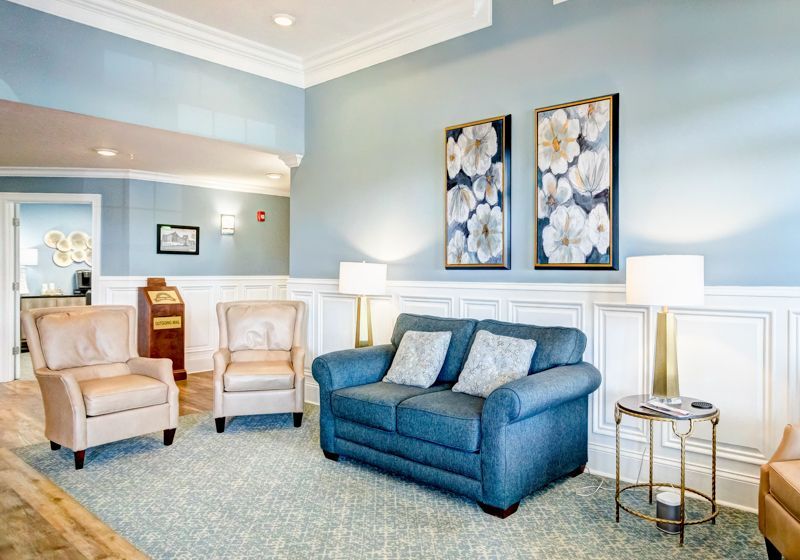 A living room with a couch , chairs , lamps and paintings on the wall.