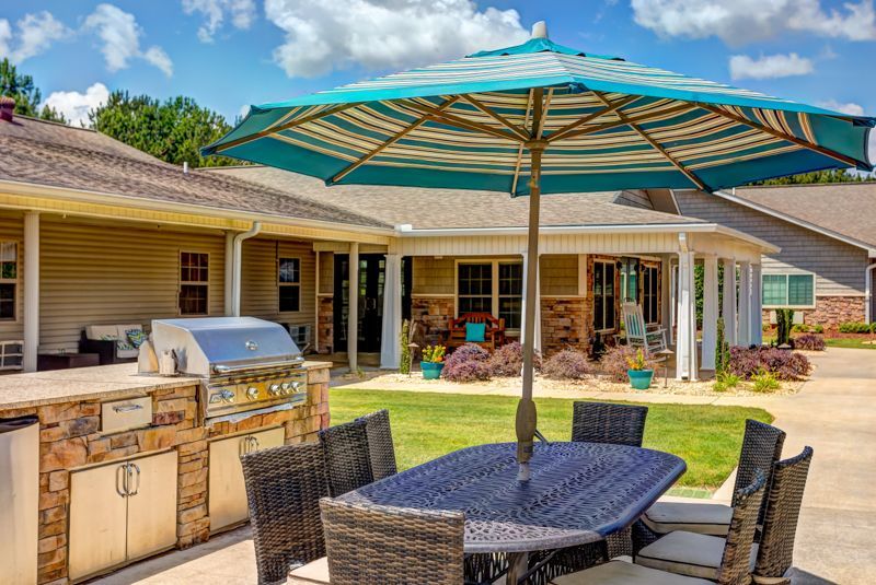 A table and chairs under an umbrella in front of a house.