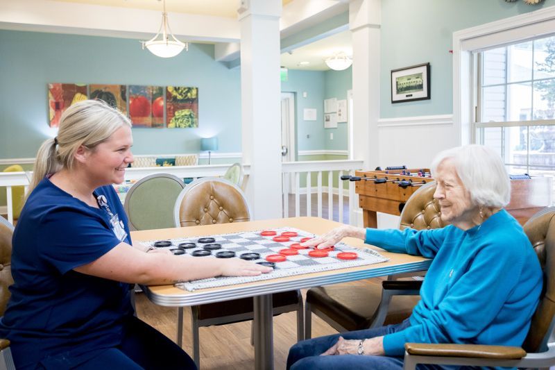 A nurse is helping an elderly woman play a game of checkers.