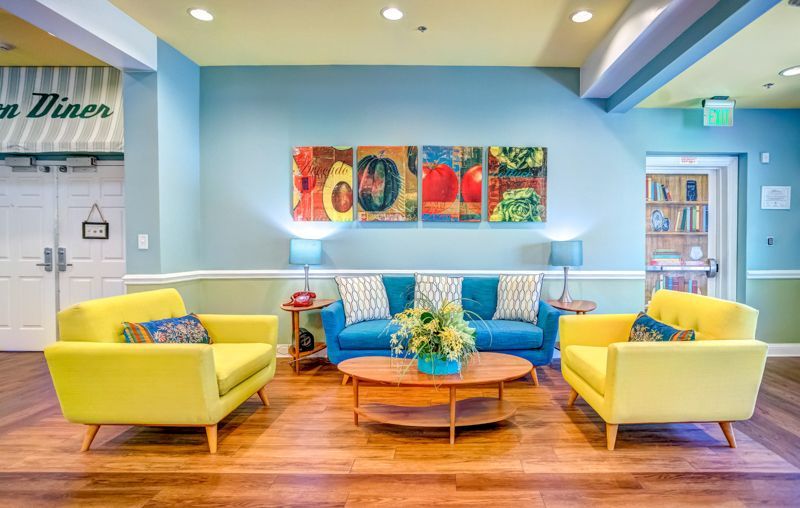 A living room with yellow chairs , a blue couch , a coffee table and a painting on the wall.