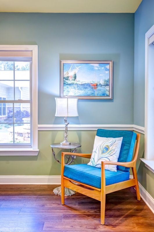 A living room with a blue chair , a lamp , and a painting on the wall.