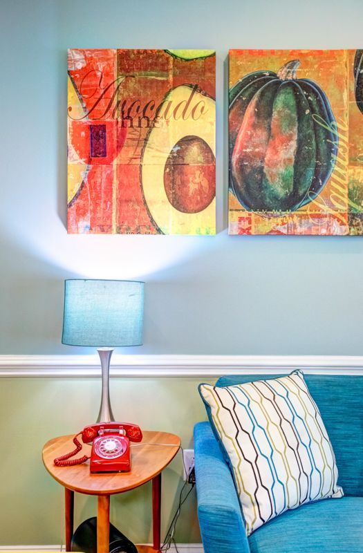 A living room with a chair , table , lamp and paintings on the wall.