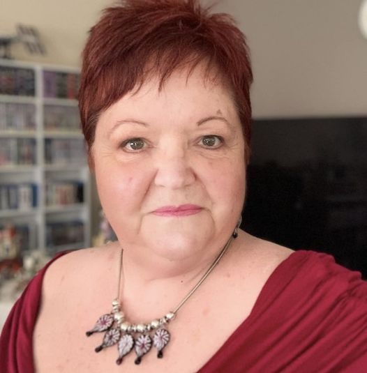 A woman wearing a red dress and a necklace looks at the camera