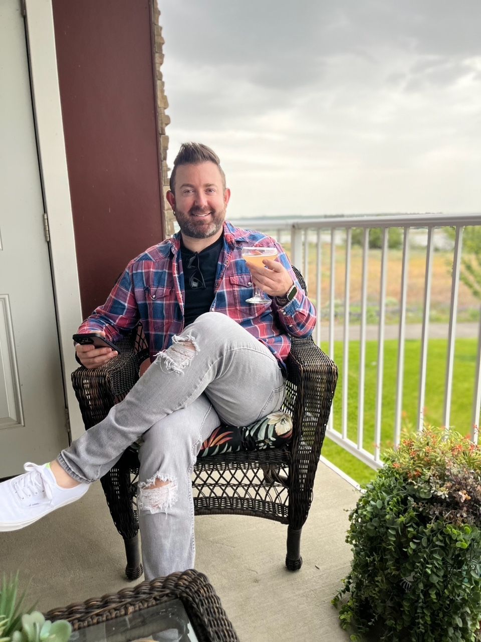 A man is sitting in a chair on a balcony holding a glass of wine.