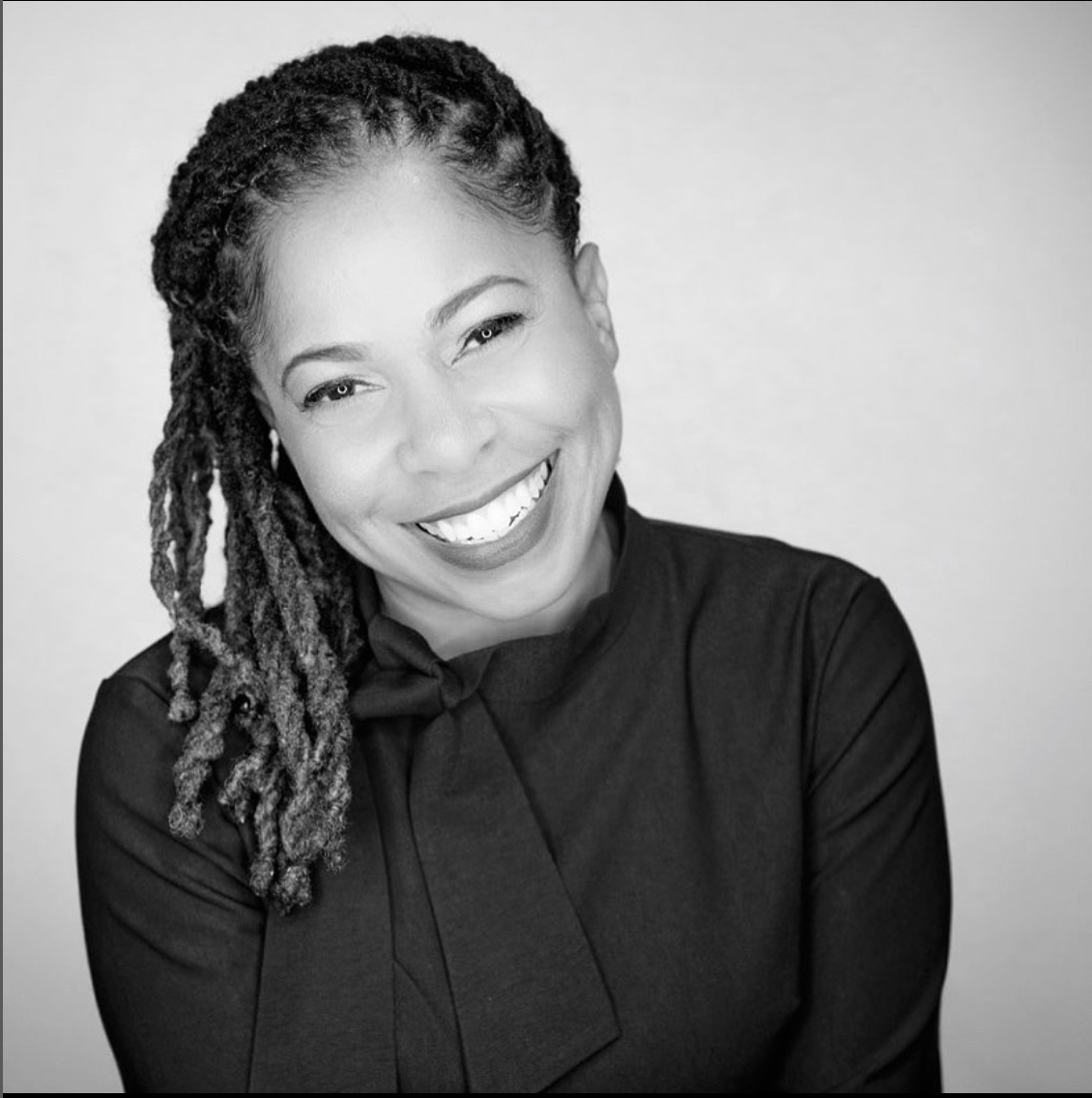 A woman with dreadlocks is smiling in a black and white photo