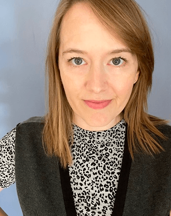A woman wearing a leopard print shirt and a gray vest is smiling for the camera.