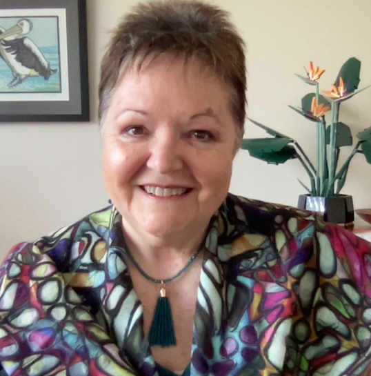 A woman in a colorful shirt is smiling in front of a picture of a penguin
