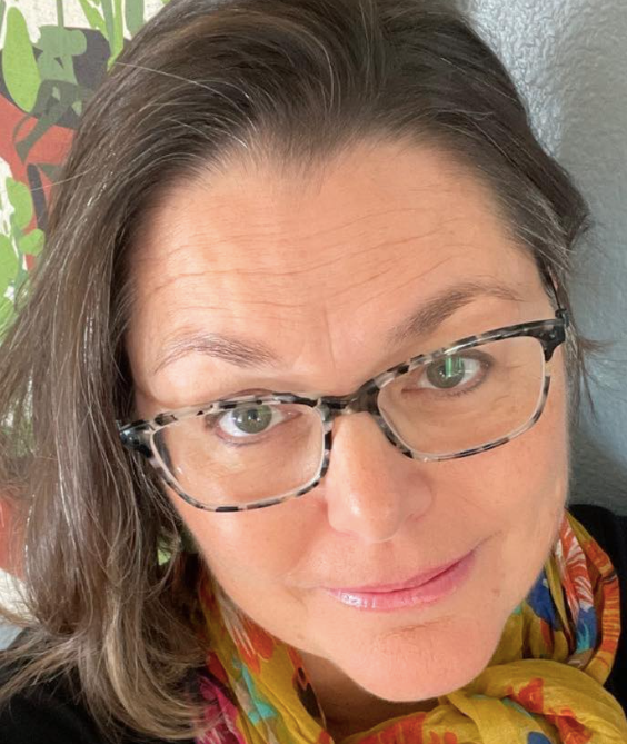 A woman wearing glasses and a scarf is smiling for the camera.
