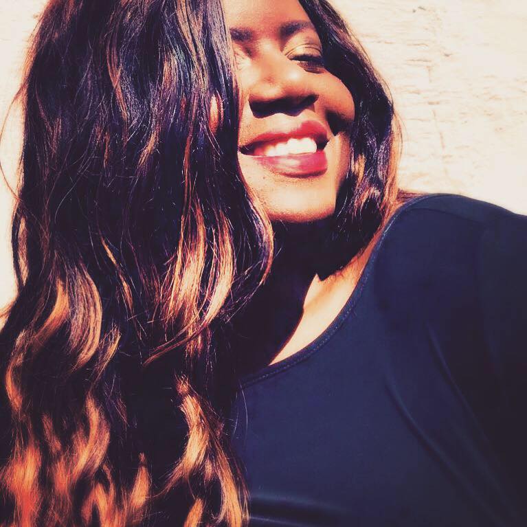 A woman with long hair is smiling and wearing a black shirt.
