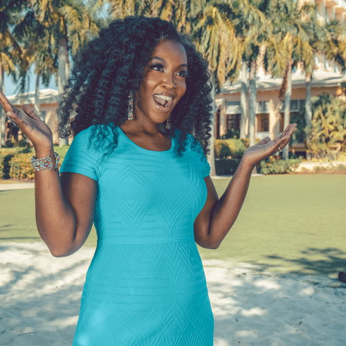 A woman in a blue dress is standing in a park with her arms outstretched.