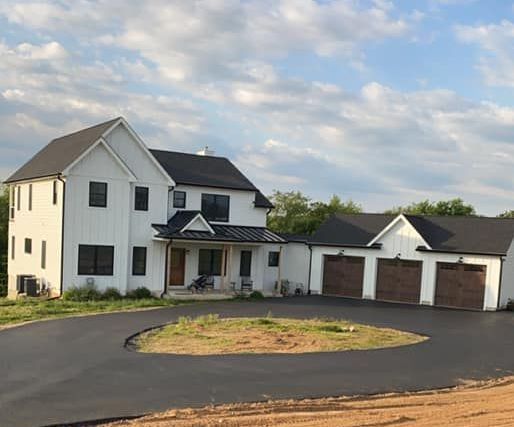 White farmhouse with black roof, black framed windows, and a three-car garage. Asphalt driveway.