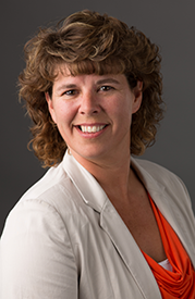 Smiling woman in a white blazer and orange top against a dark gray background