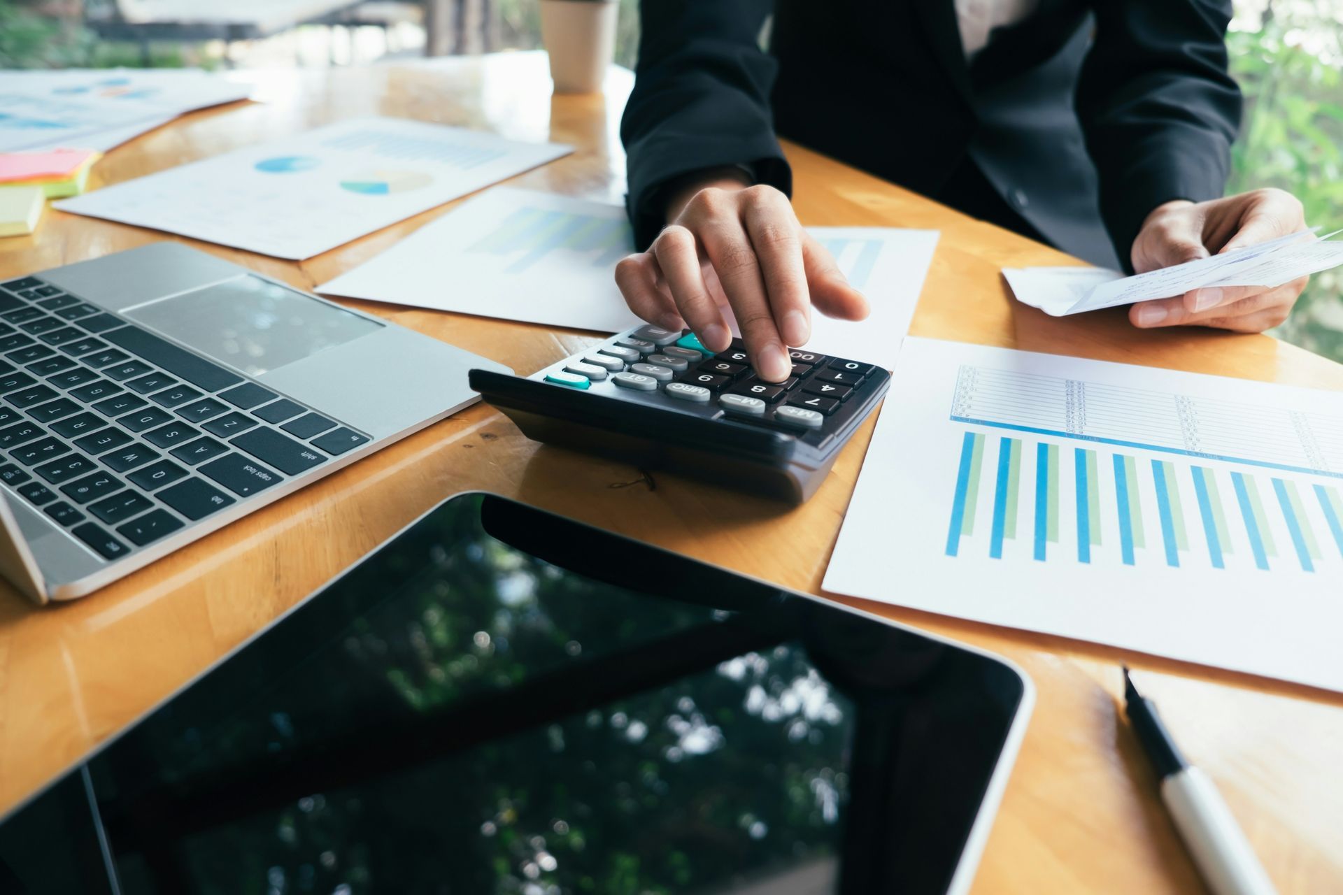 Hands using a calculator at a desk with laptop and printed charts in a business meeting