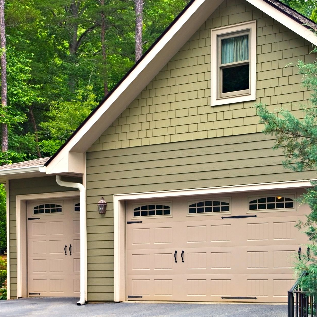 Two-car garage and side entry on a beige house with green siding, surrounded by trees