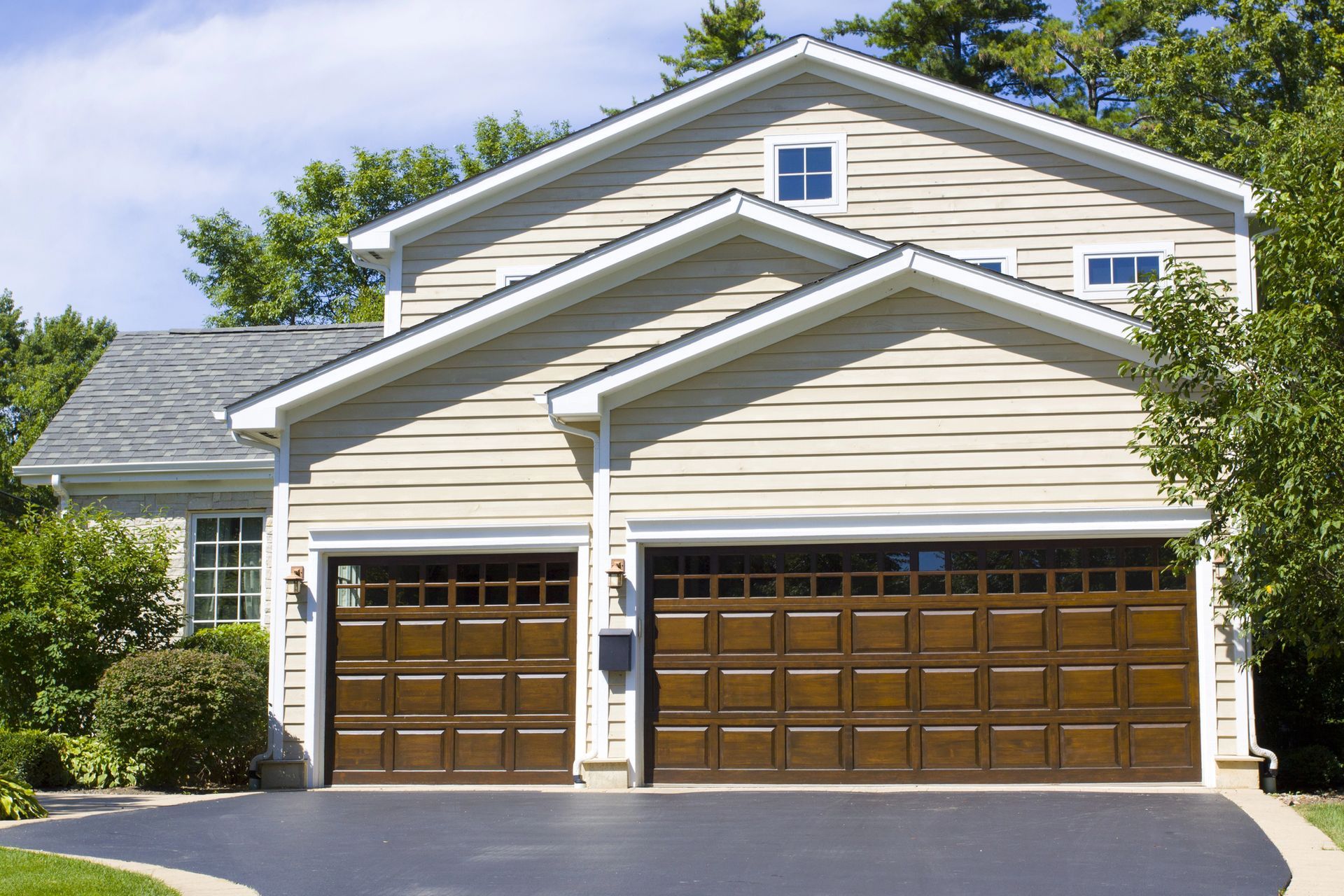 Suburban two-story house with beige siding, white trim, and a brown double garage door under a bright sky