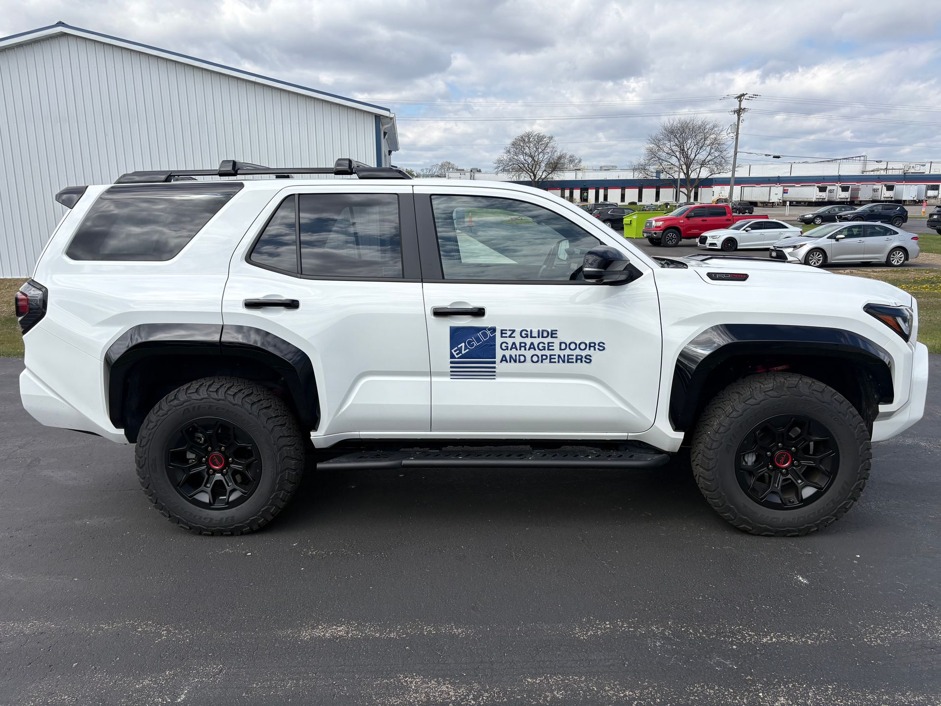 White off-road SUV with black wheels parked beside a metal building in a lot