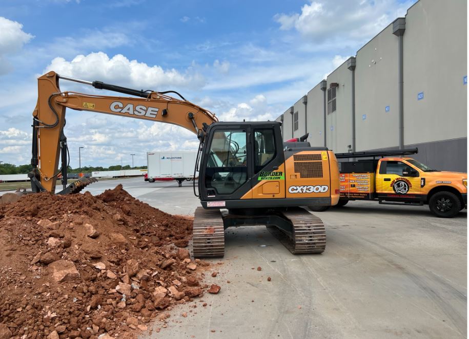 A case excavator is sitting in a parking lot next to a truck.
