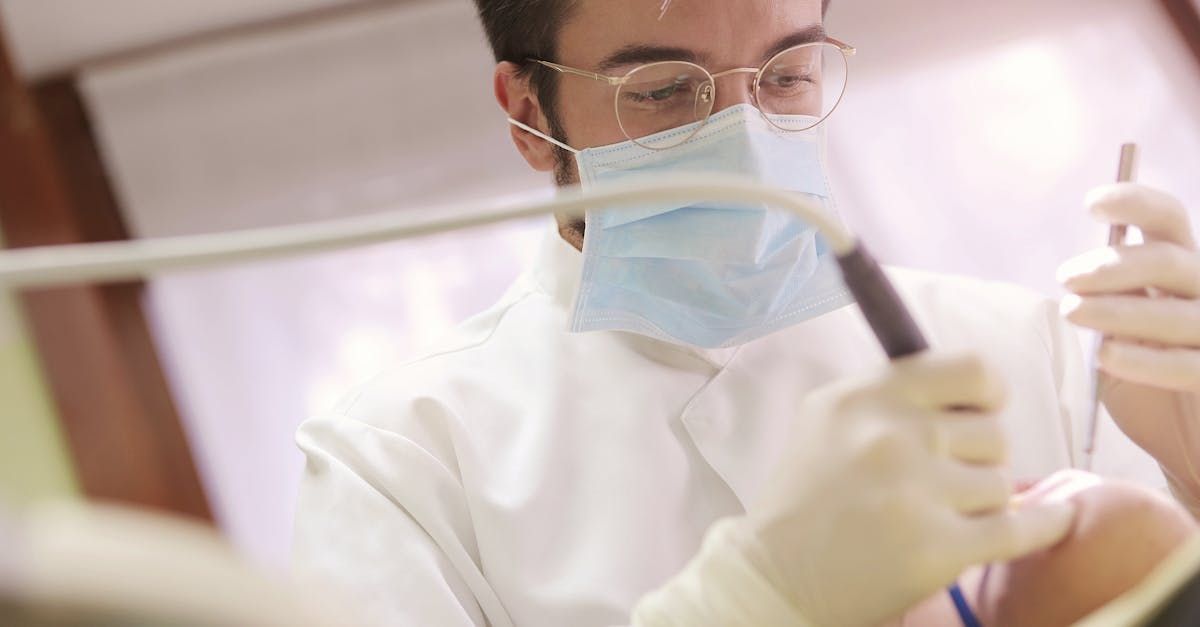 Un dentiste portant un masque et des gants examine les dents d'un patient à l'aide d'un instrument dentaire.