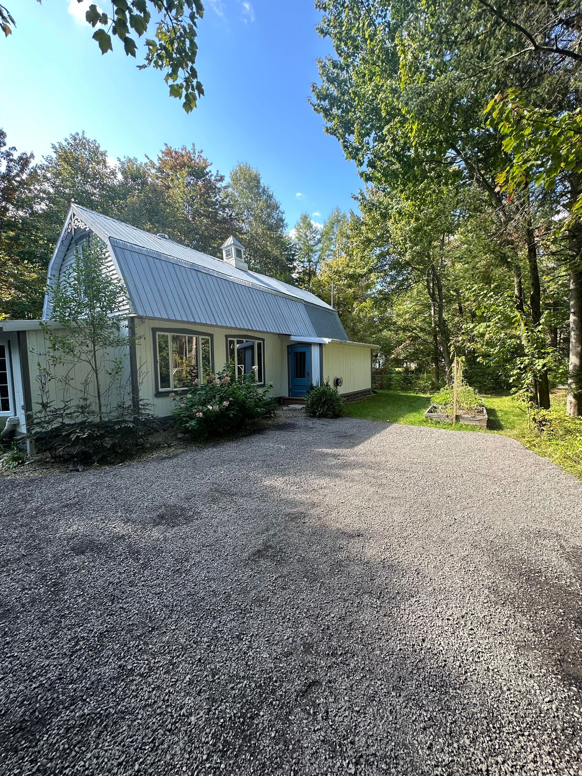 Une maison blanche avec une allée de gravier devant elle entourée d'arbres.