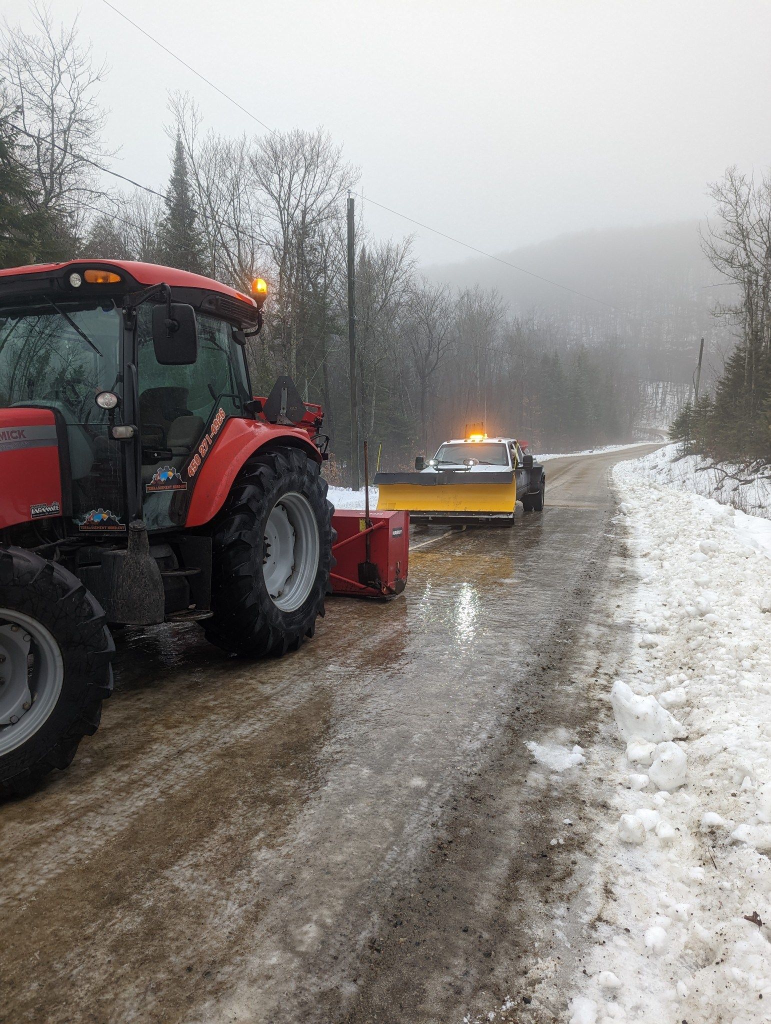 Un tracteur rouge roule sur une route enneigée à côté d'un chasse-neige.