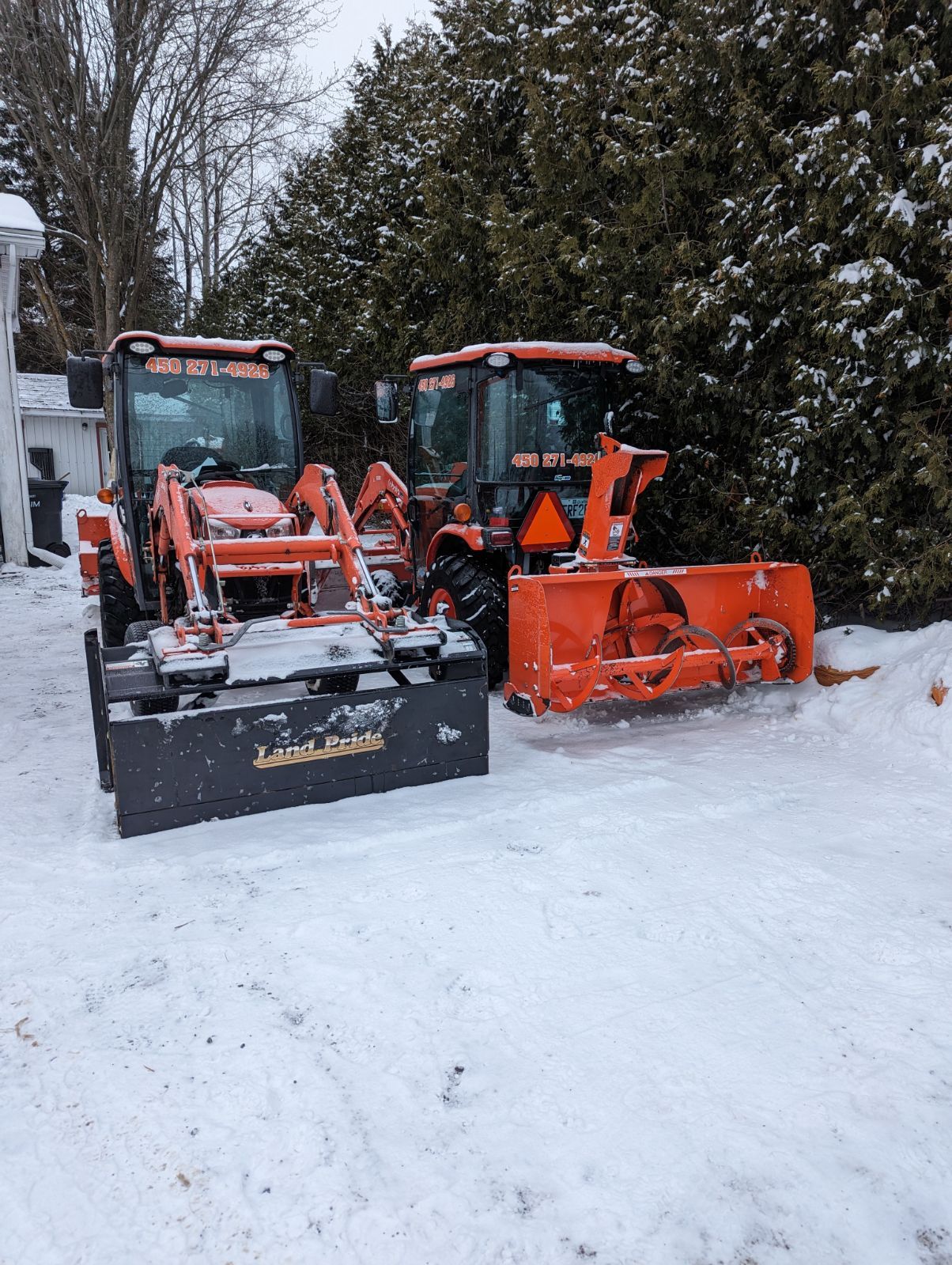 Deux tracteurs orange et un chasse-neige sont garés dans la neige.