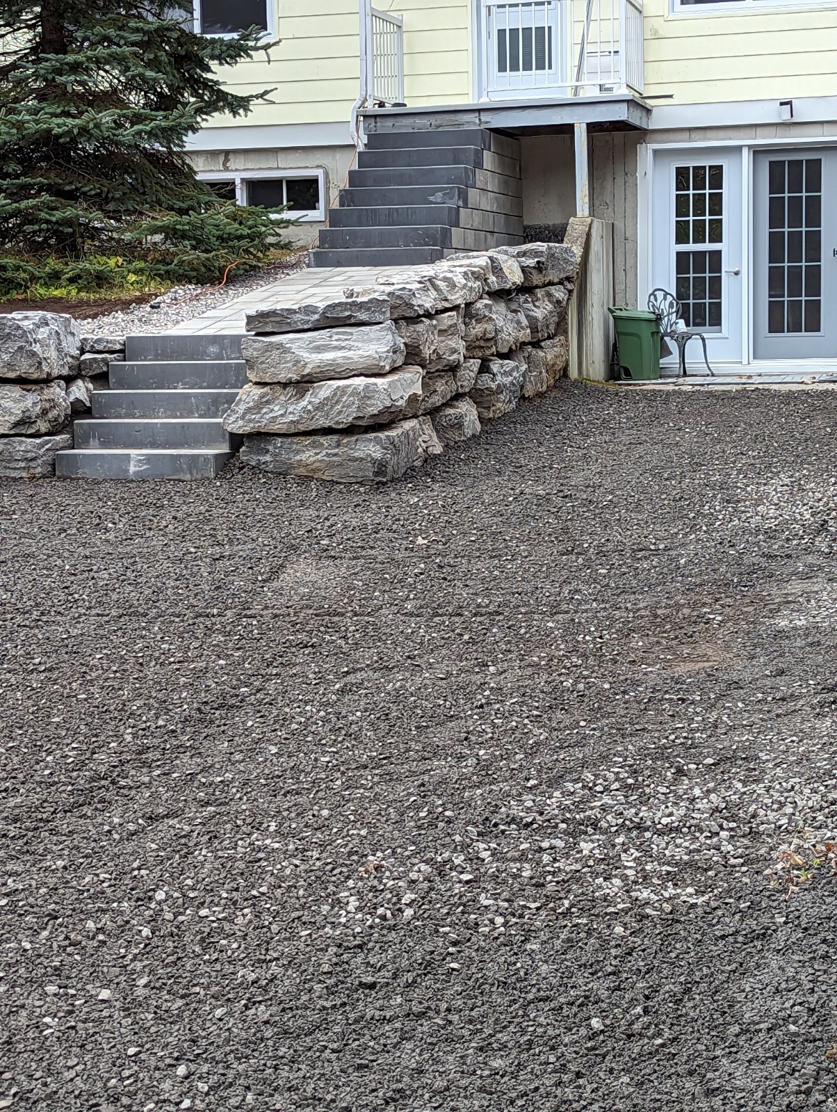 Une allée de gravier devant une maison avec des escaliers et un mur de pierre.
