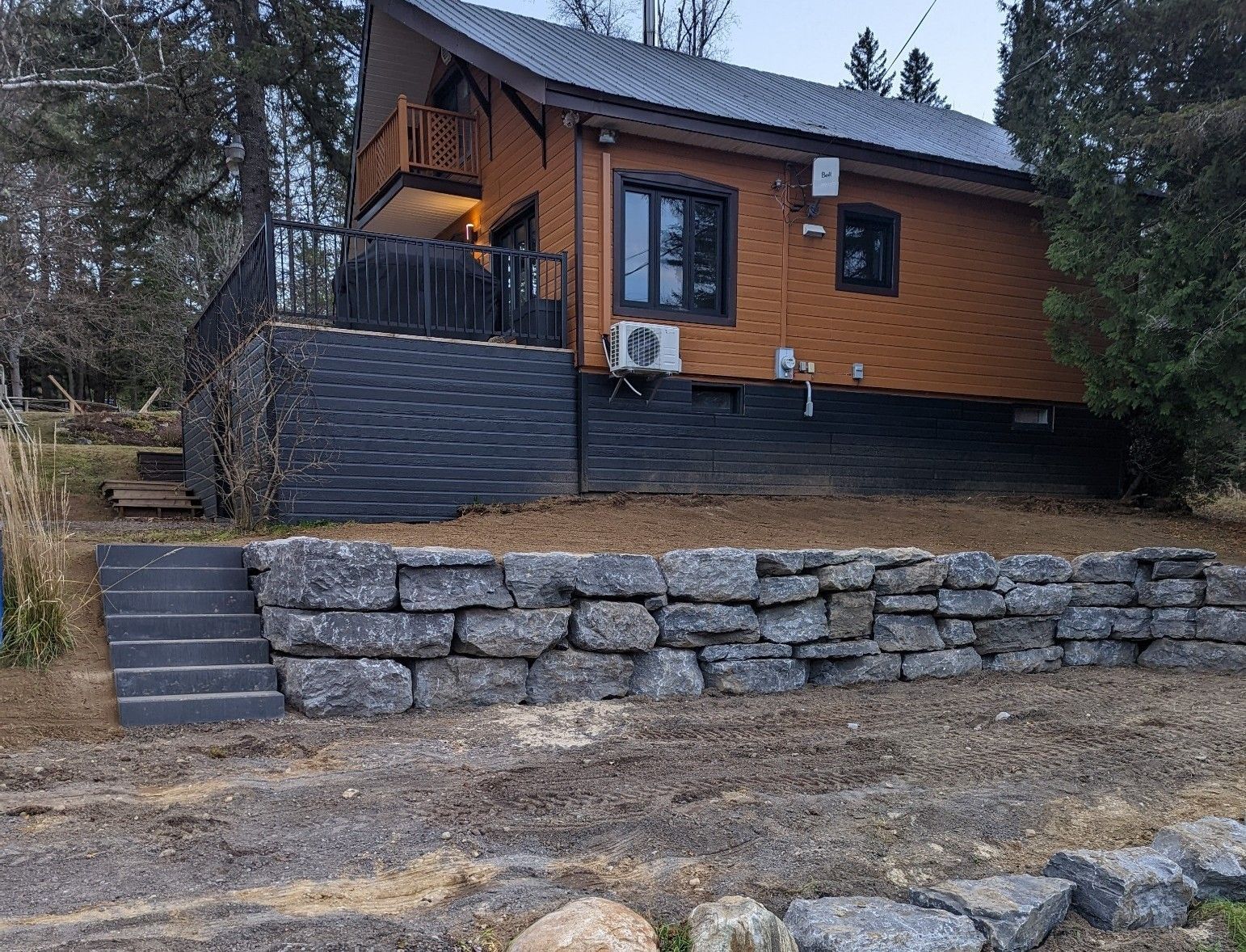 Une maison est située au sommet d'une colline à côté d'un mur de pierre.