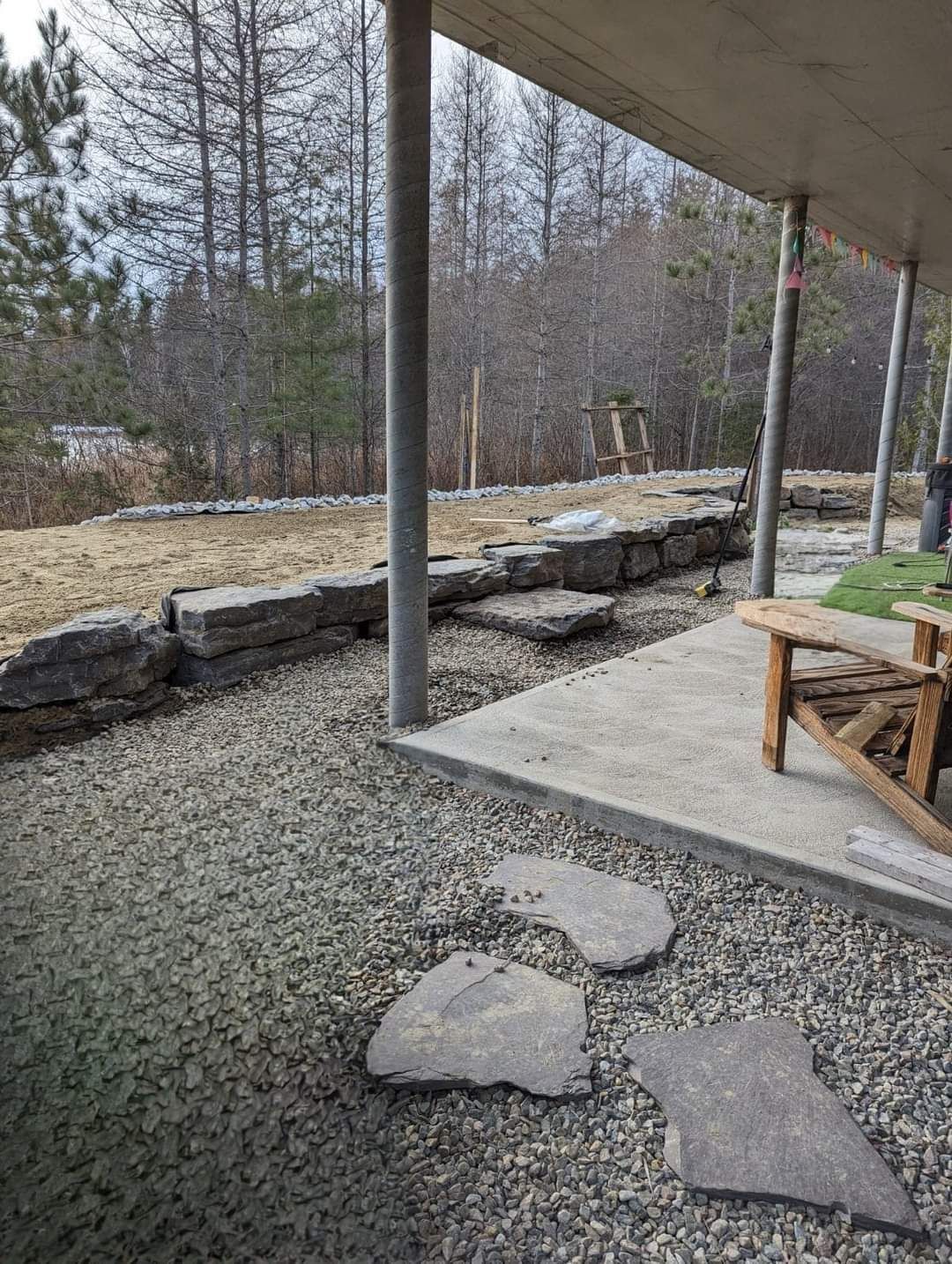 Une chaise à bascule est posée sur une terrasse en gravier sous un porche couvert.