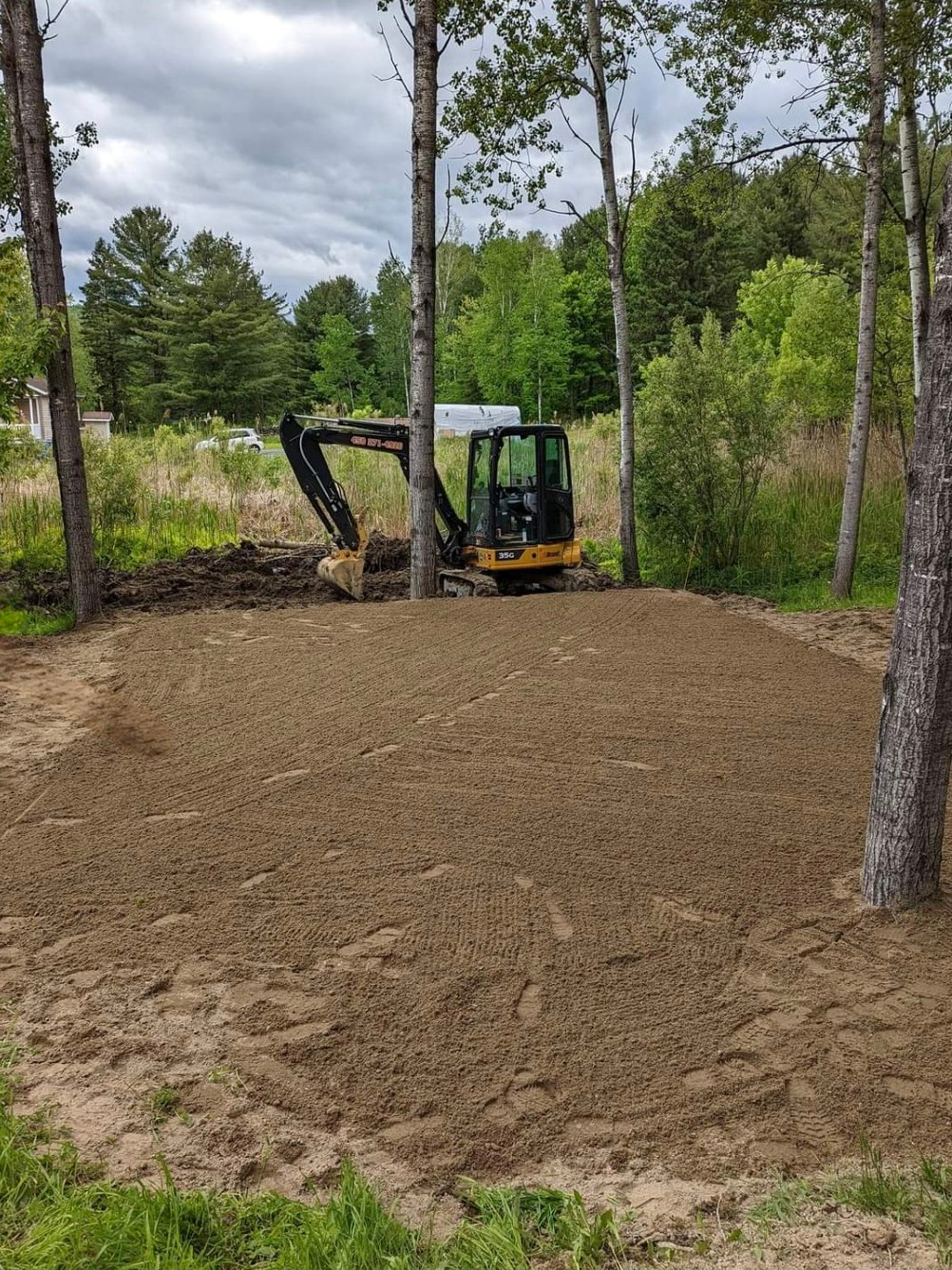 Une petite excavatrice travaille sur un champ de terre entouré d'arbres.