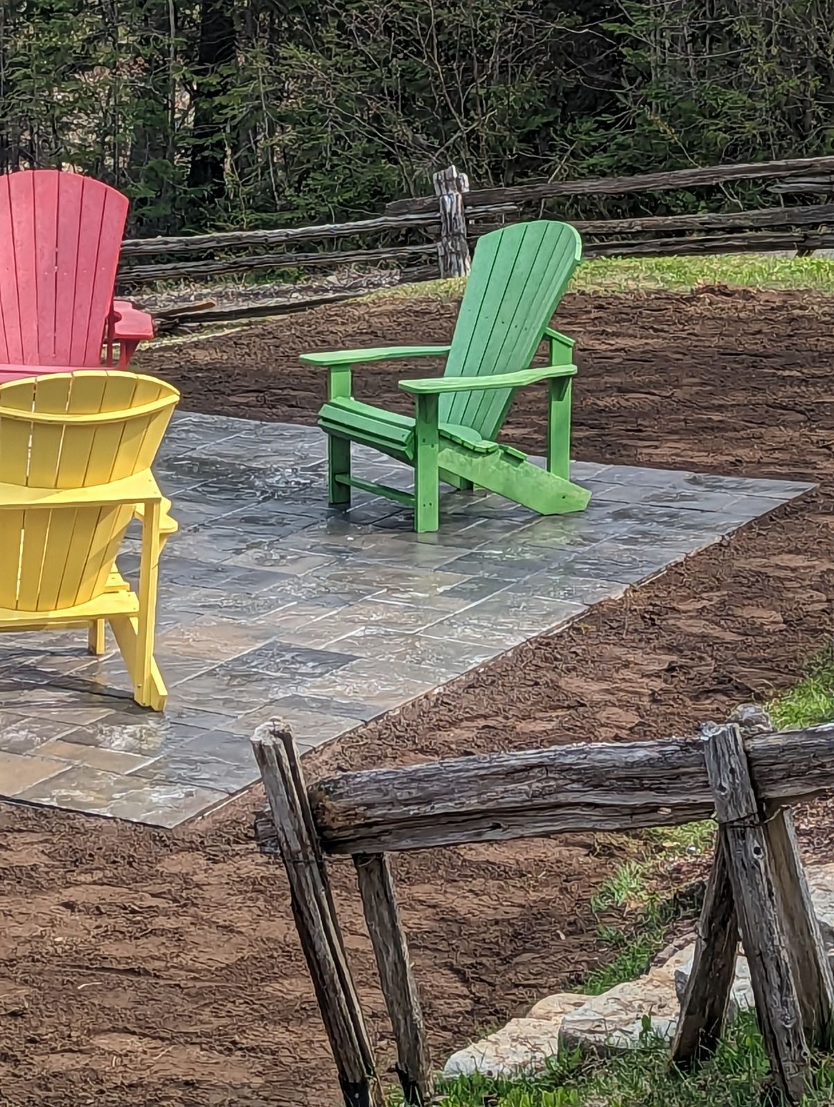 Trois chaises de jardin colorées sont assises sur un patio à côté d'une clôture en bois.