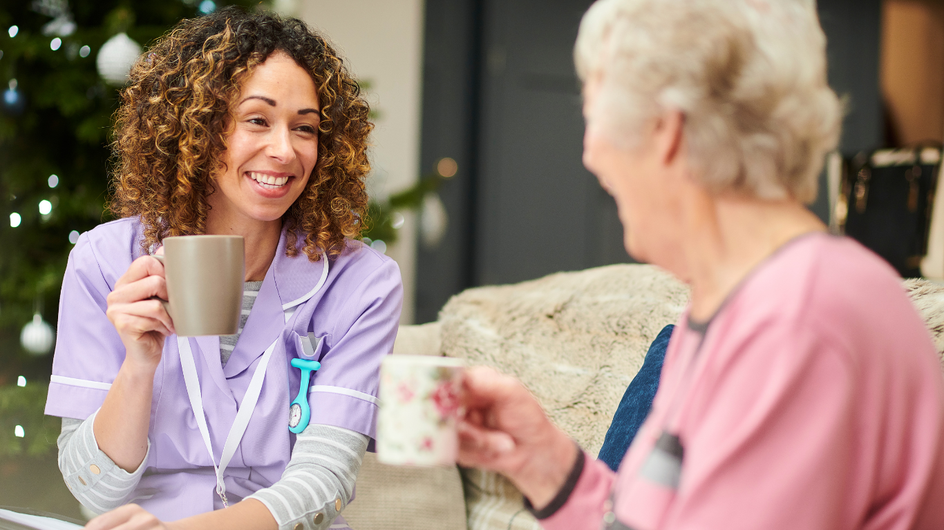 Two women smiling and chatting while holding mugs in a living room