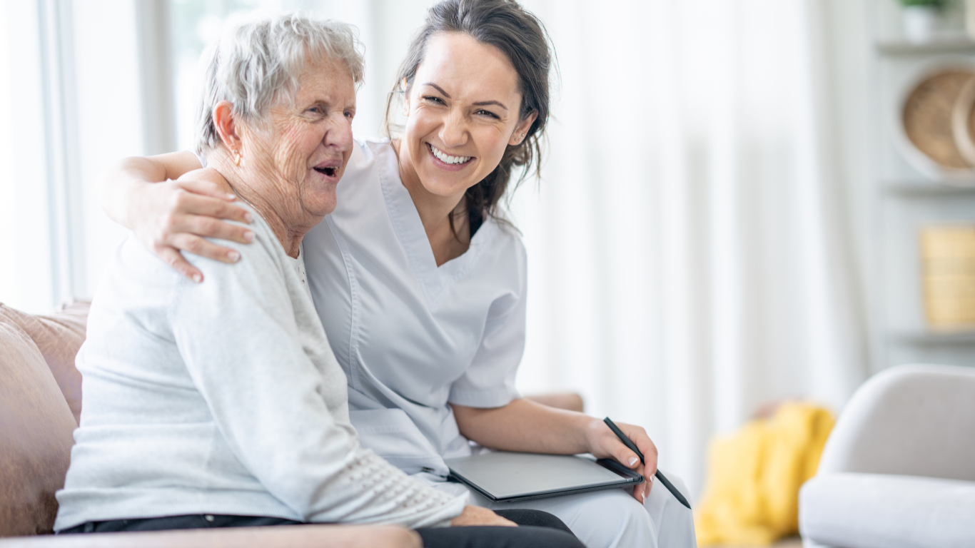 Two smiling people sitting on a couch in a bright living room, one embracing the other