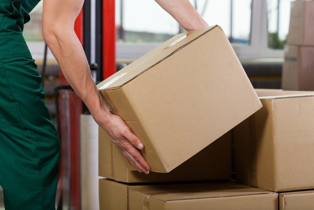 A Man is Lifting a Cardboard Box in a Warehouse — West End Cash Store In Proserpine, QLD