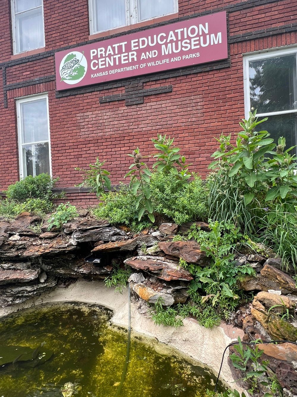 A pond in front of a brick building with a sign that says pratt education center and museum.