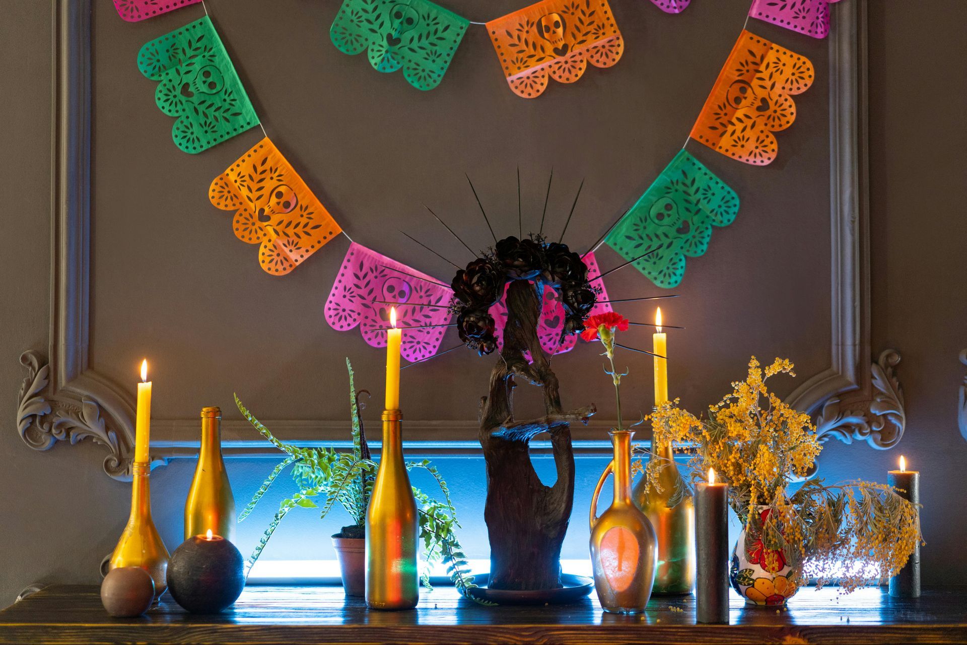 Colorful Day of the Dead altar. Paper banner, candles, and floral arrangements on a dark surface.