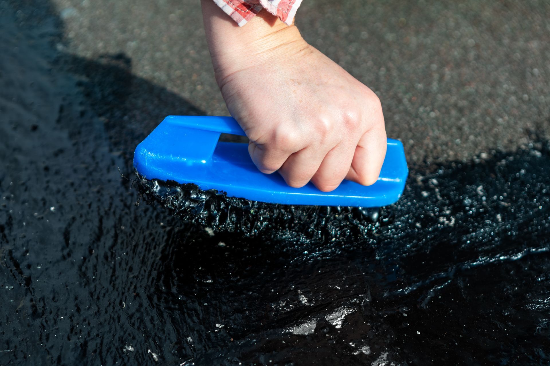 Hand applying waterproofing sealant to a surface with a blue applicator tool.