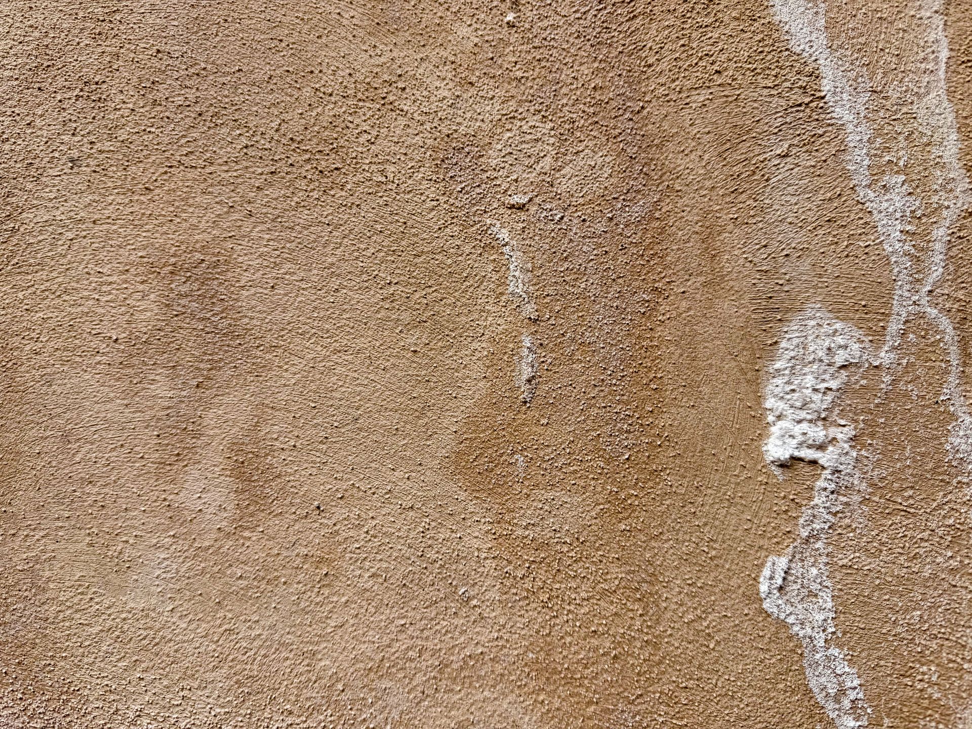 Light brown wall with faint stains and rough white patches along the textured surface. Light brown wall with faint stains and rough white patches along the textured surface.