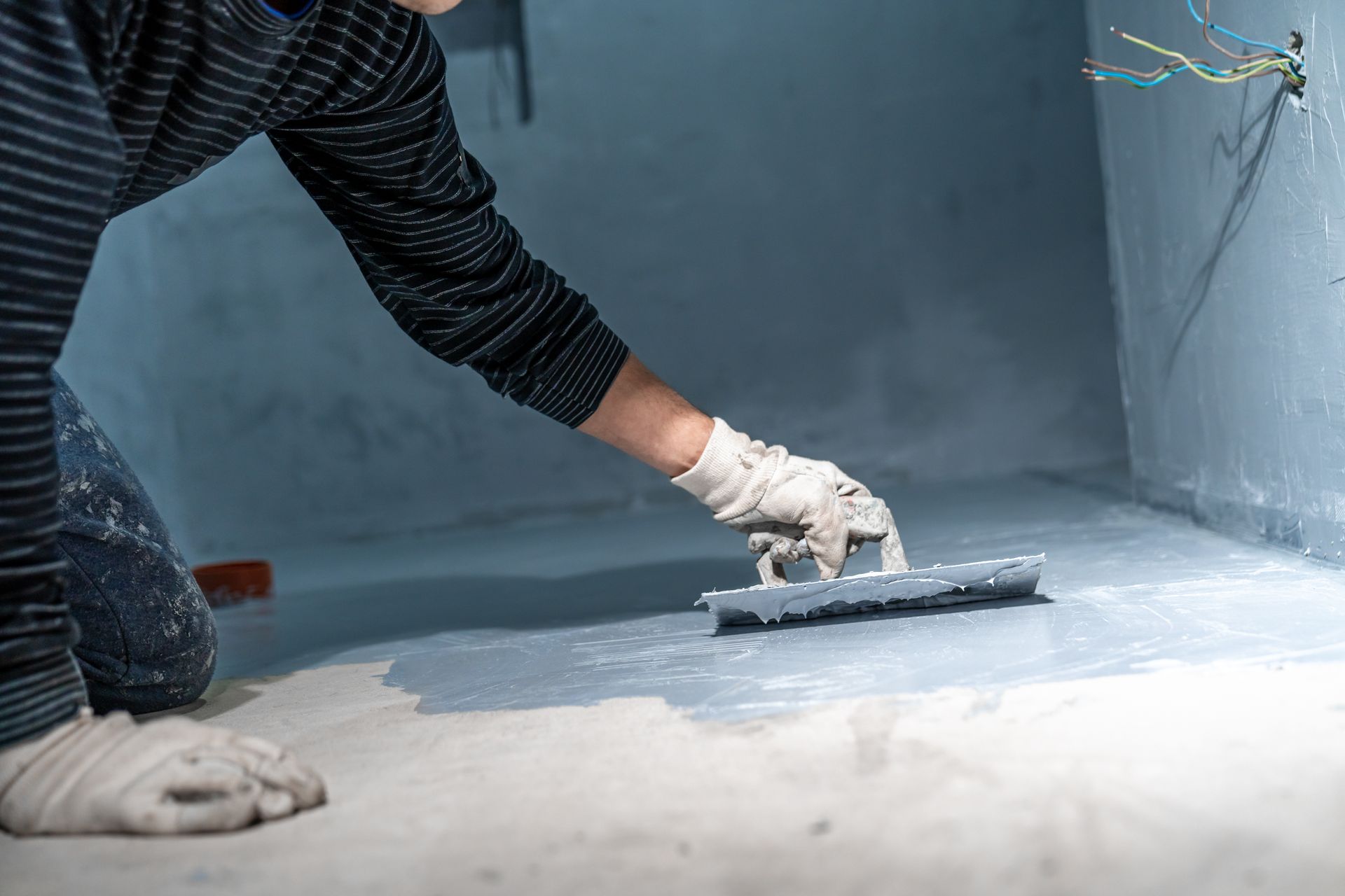 Gloved hand trowels waterproof coating onto a basement floor and wall corner.