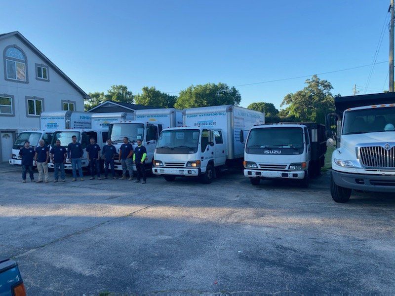 Group of people standing in front of several service trucks outside a building.