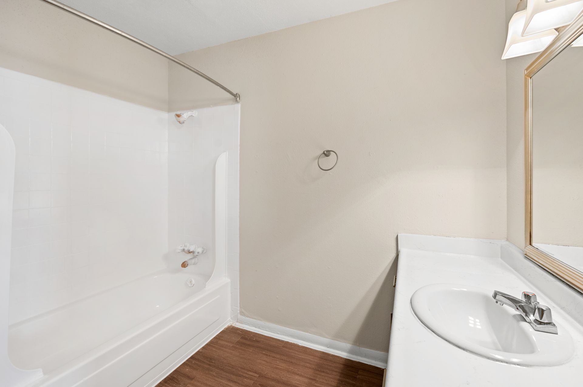 Bathroom with white tub/shower, vanity, and brown floor. Beige walls, chrome fixtures.