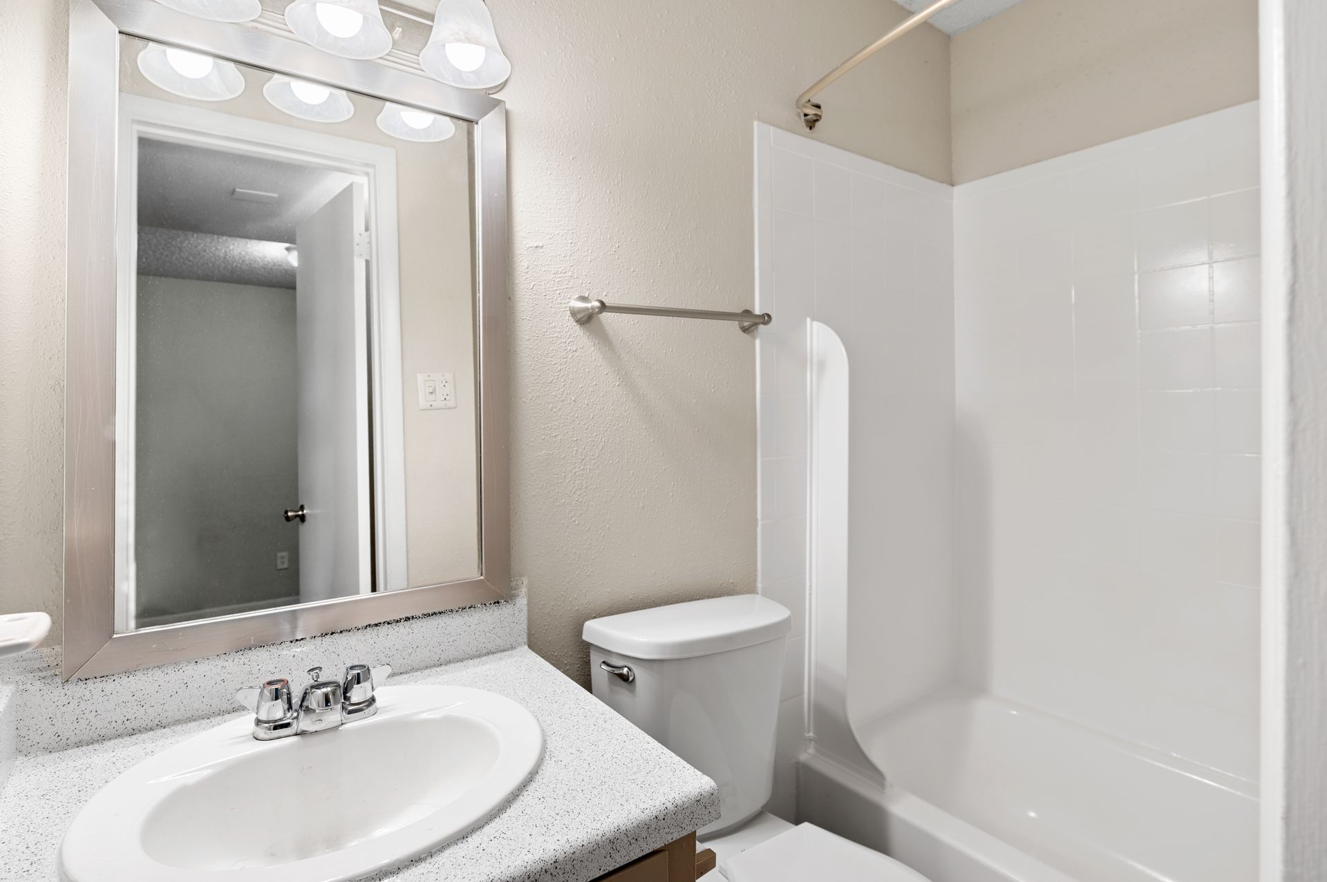 Bathroom with white fixtures, vanity, toilet, shower/tub combo, and wall-mounted mirror.