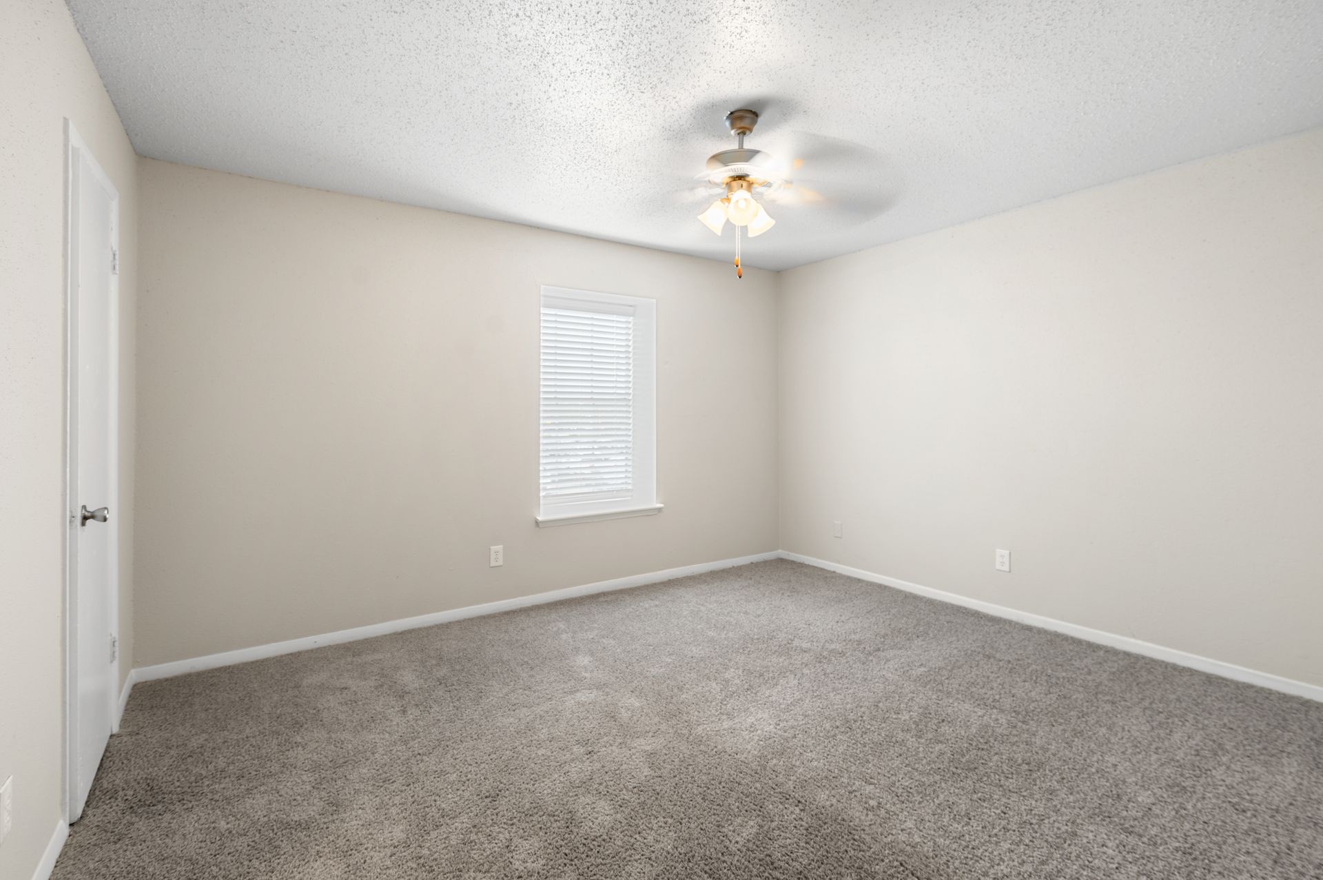 Empty bedroom with beige walls, gray carpet, and a ceiling fan.
