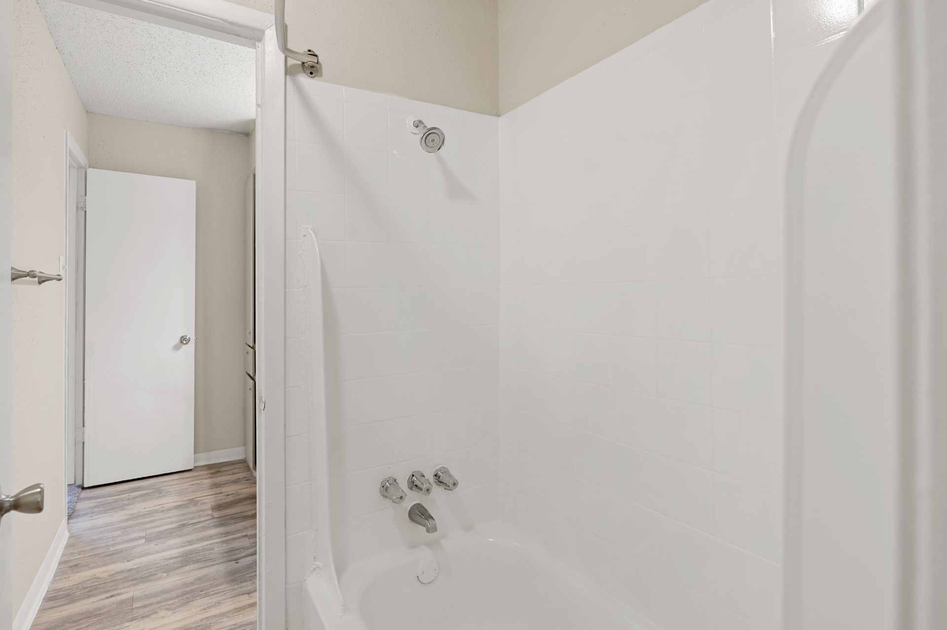 White bathroom with a shower/tub combo, silver fixtures, and a doorway.