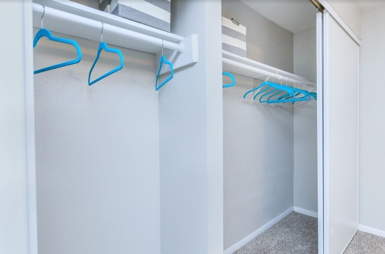 Empty walk-in closet with white walls, sliding doors, and blue hangers.