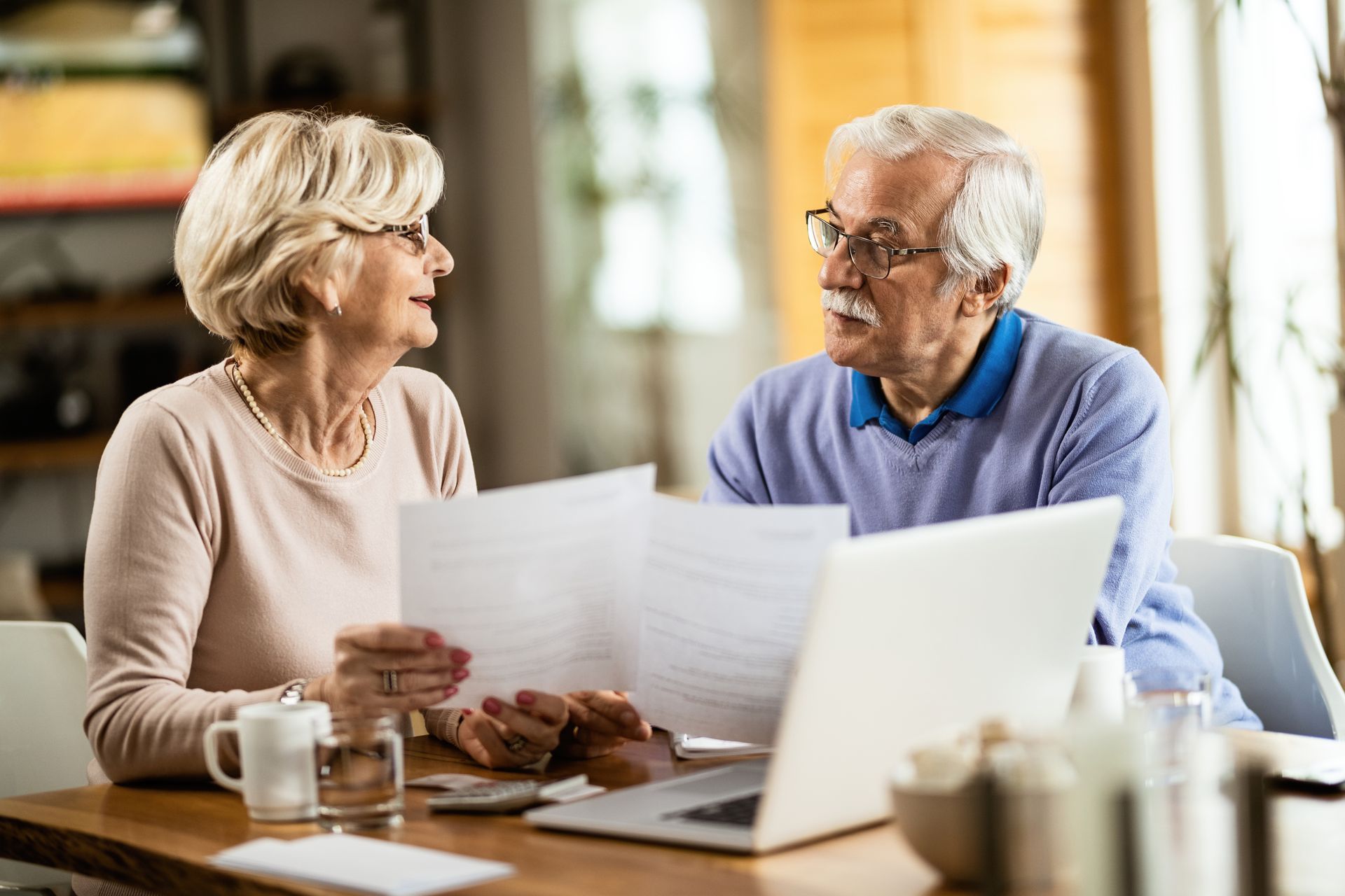 Senior couple reviewing documents with a laptop at a table, discussing finances.Icon